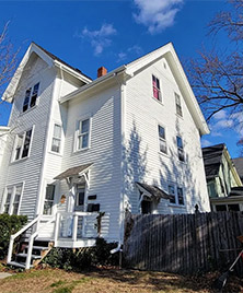 A white two story house with a white picket fence in need of exterior painting services at competitive prices.