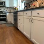 A kitchen with white cabinets and hardwood floors showcased in a house painting photo gallery.