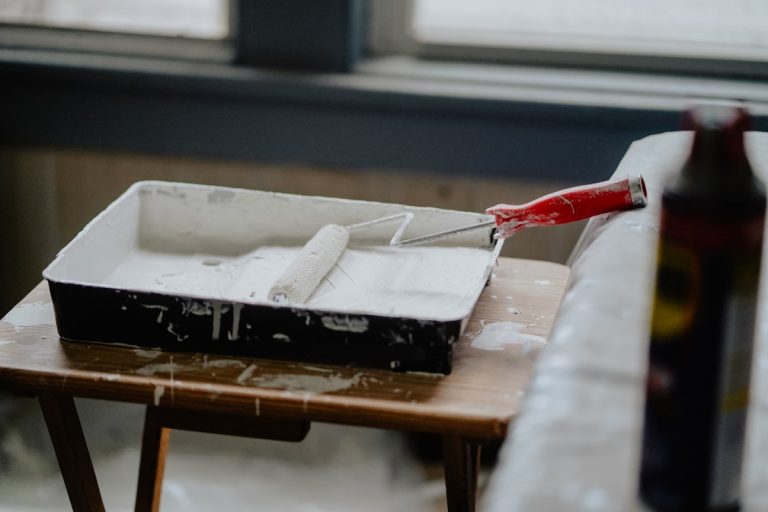 White paint roller and tray resting on a wooden stool during an interior house painting project in Rhode Island