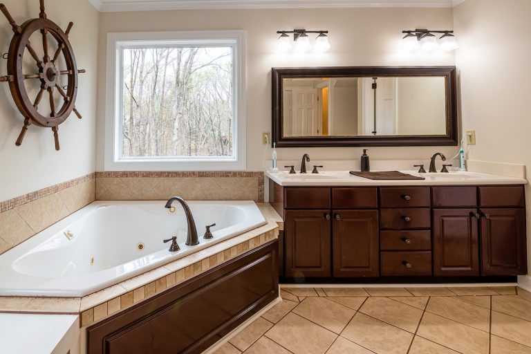 Master bathroom with warm beige painted walls dark wood vanity double sinks jetted tub and nautical decor in a Rhode Island home
