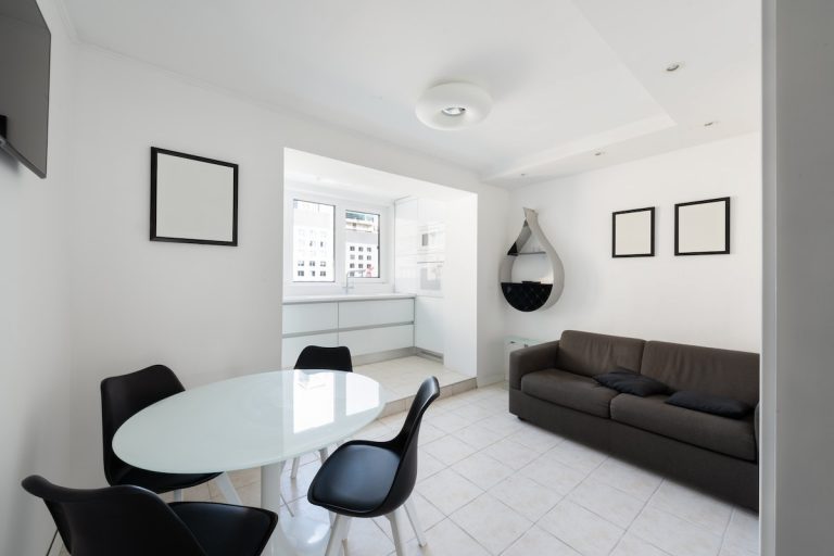 Minimalist apartment living and dining area with crisp white painted walls crown molding tile floors and black furniture in Rhode Island