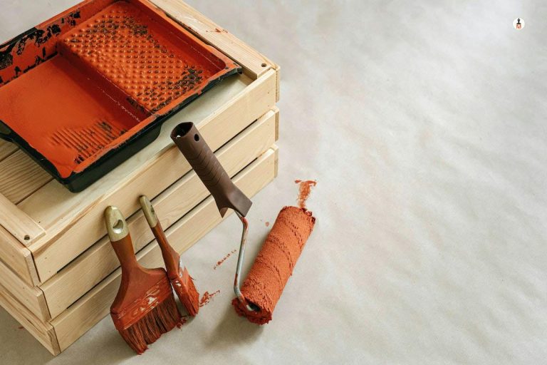 A paint brush is sitting on a wooden crate as painters wear white clothes.