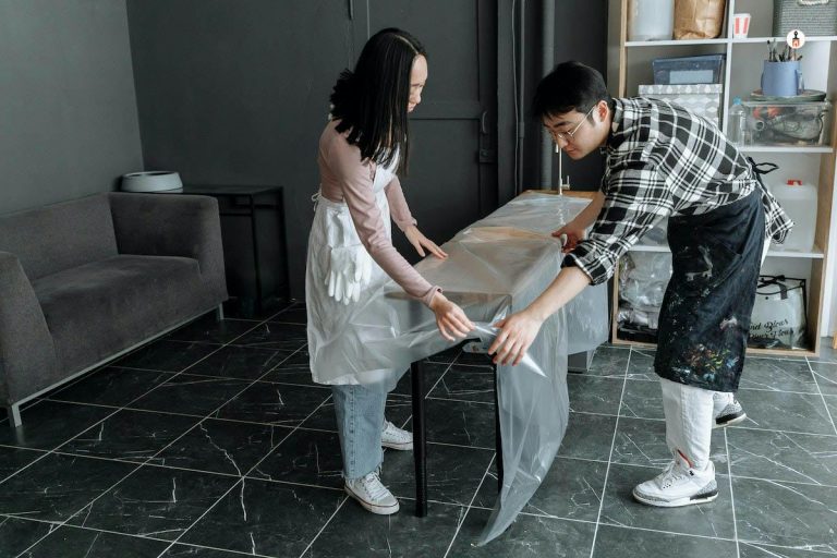 Two people wrapping furniture in plastic sheeting to protect it before an interior painting project in a Rhode Island home