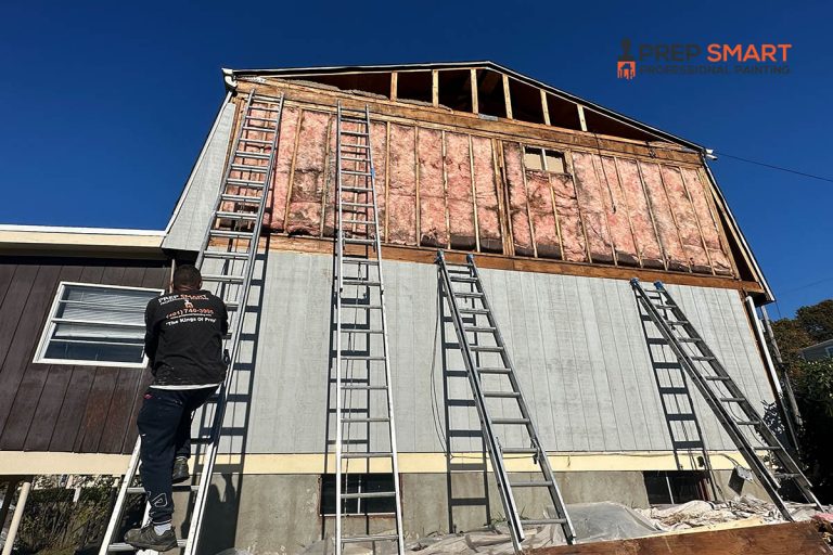 Prep Smart crew member on a ladder prepping a home exterior with exposed framing and primer coat before painting in Rhode Island