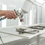 Professional painter using a spray gun to paint a cabinet door flat in a spray booth