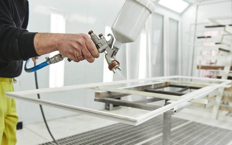 Professional painter using a spray gun to paint a cabinet door flat in a spray booth