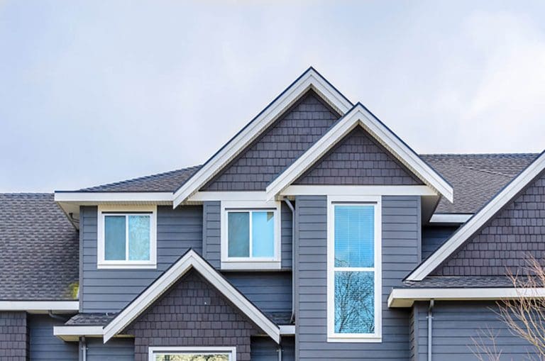 Two-story home with blue-gray siding, white trim, and gabled roof illustrating the best time to schedule exterior painting in Providence