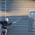 Exterior painter applying paint to home siding in cold conditions, illustrating how winter weather affects exterior painting in Providence