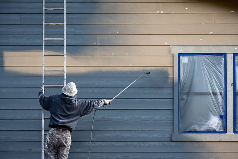 Exterior painter applying paint to home siding in cold conditions, illustrating how winter weather affects exterior painting in Providence