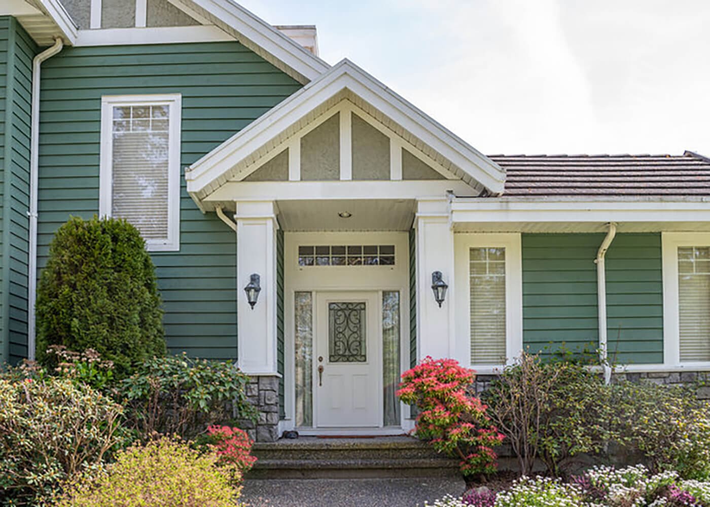 Home exterior with green siding and white trim surrounded by spring landscaping ready for exterior painting
