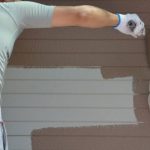 Painter applying brown exterior paint to horizontal siding, illustrating what to expect during exterior house painting in Warwick.
